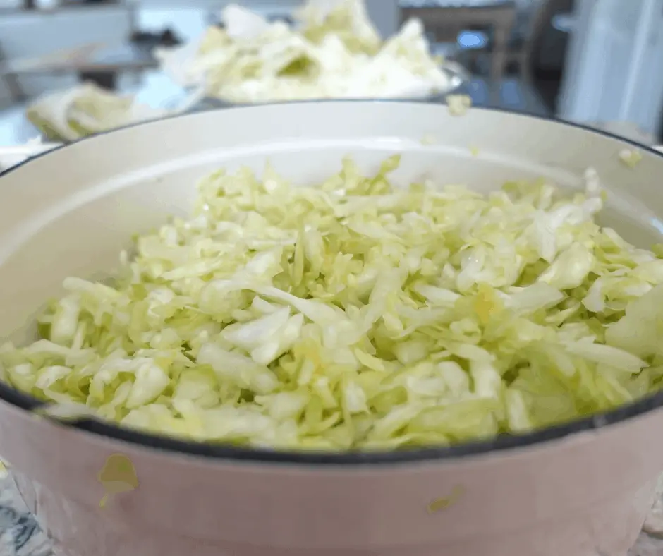 cabbage massaged into sauerkraut and brine inside a white dutch oven with cabbage cores in the background