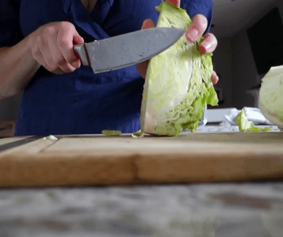 bright green cabbage cut in quarters on wooden cutting board  using chefs knife