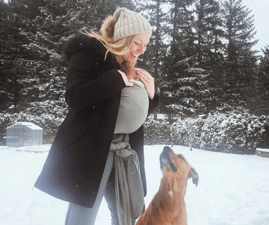 first time mom wearing her baby in a boba wrap in the snow with her dog