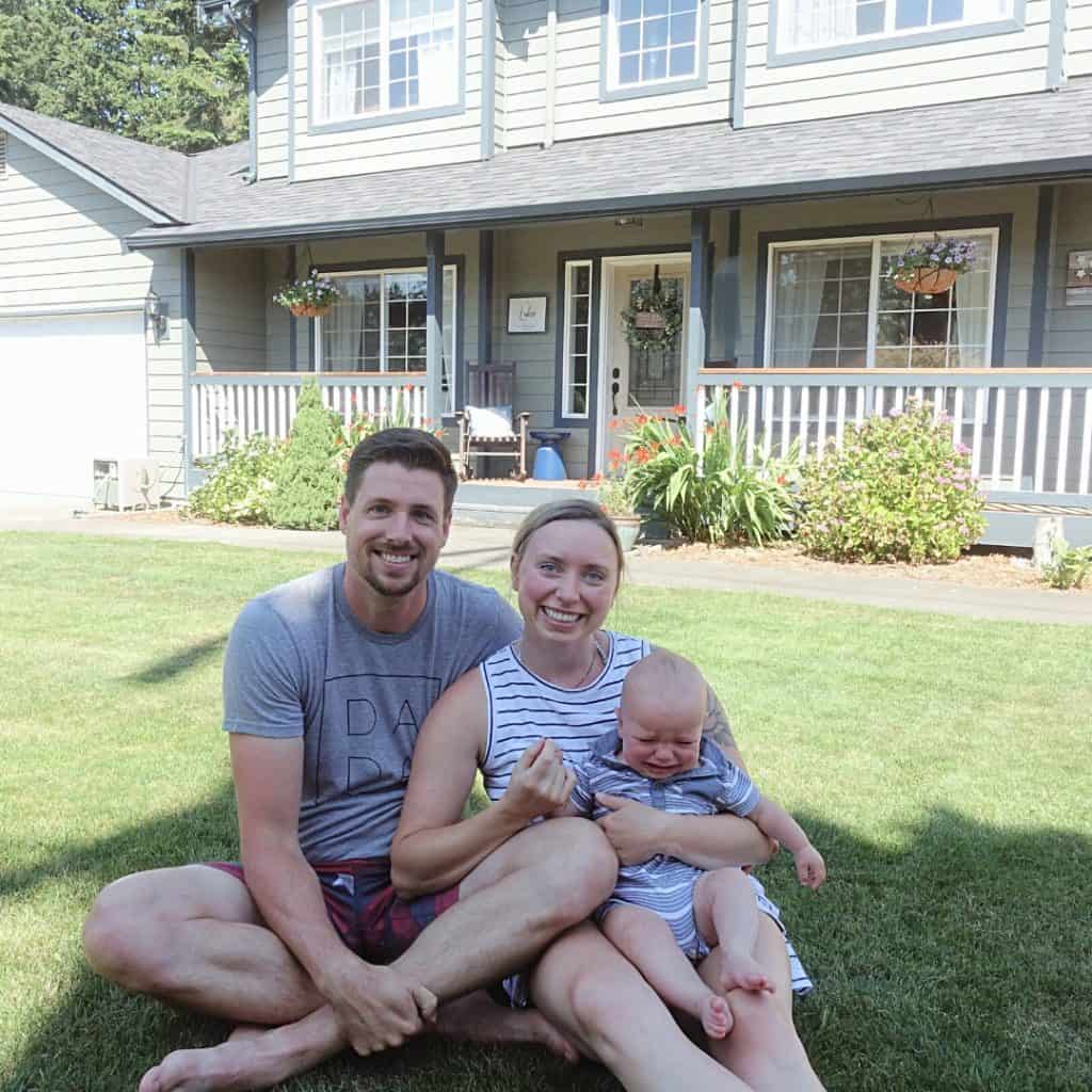 first time parents with their baby on the lawn in front of their homestead