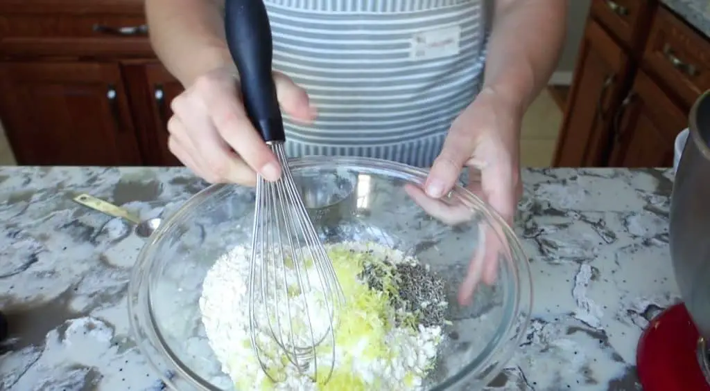 mixing flour lemon and lavender with a whish wearing an apron
