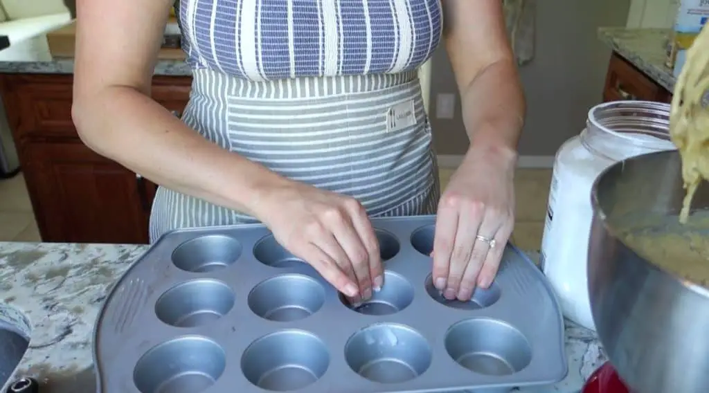 greasing a muffin tin with coconut oil wearing apron