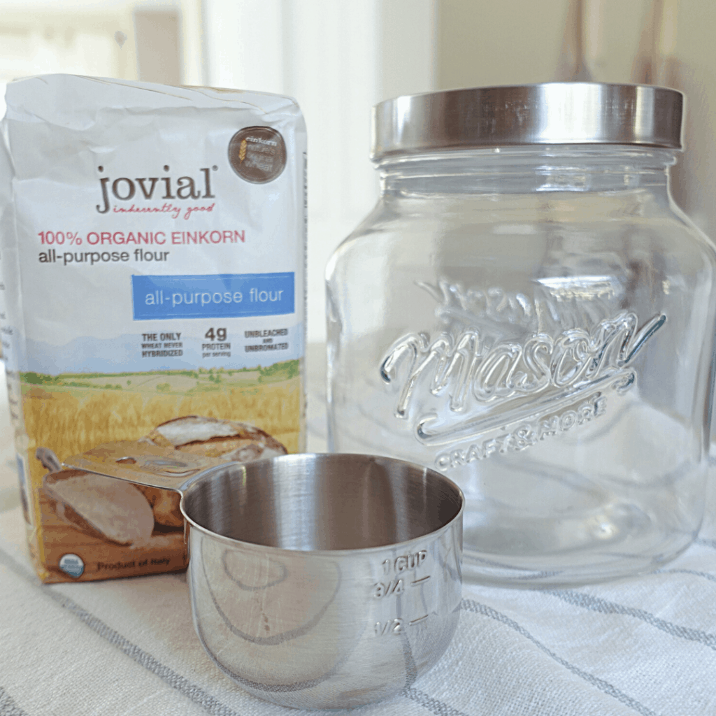 materials to make sourdough starter jovial einkorn flour mason jar and measuring cup on top of tea towel