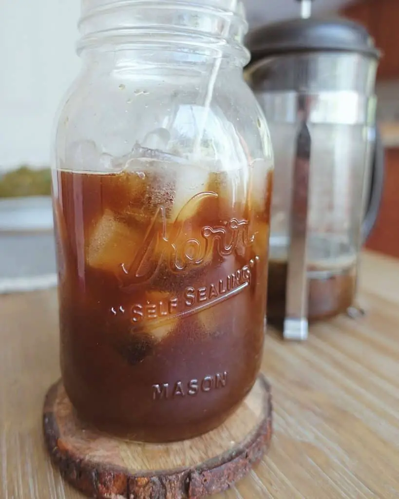 iced coffee in a mason jar black with no cream in front of a french press