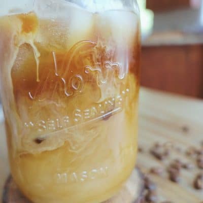iced coffee with cream in mason jar with coffee beans surrounding it