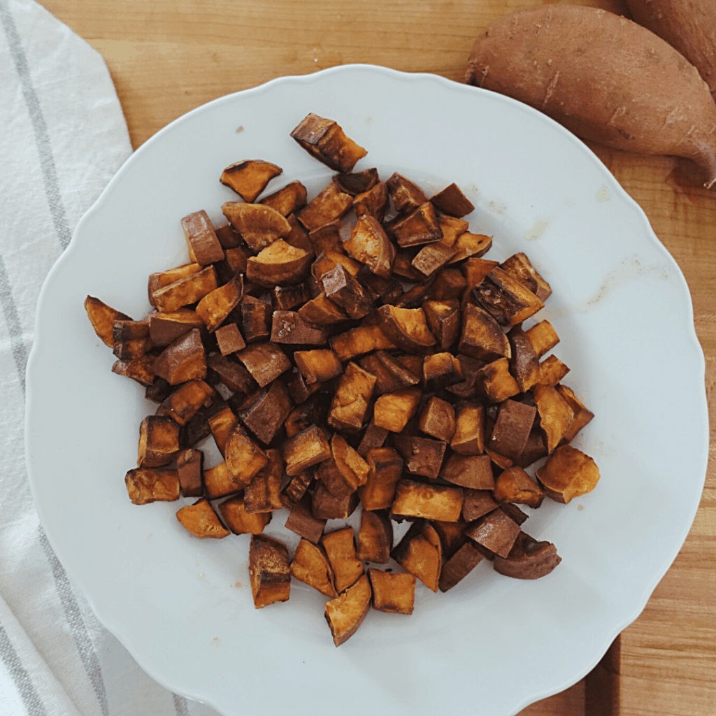 crispy sauteed sweet potatoes on white plate with tea towel and whole sweet potatoes in background