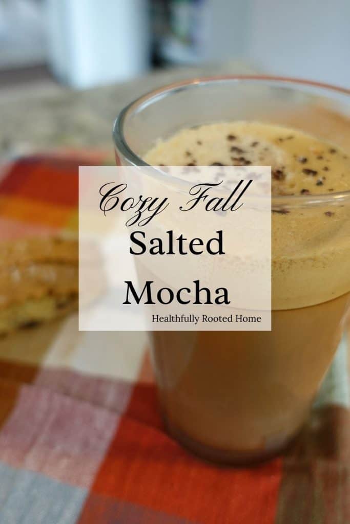 Cozy fall salted mocha in a glass coffee cup with two biscotti sitting on a red checkered tea towel