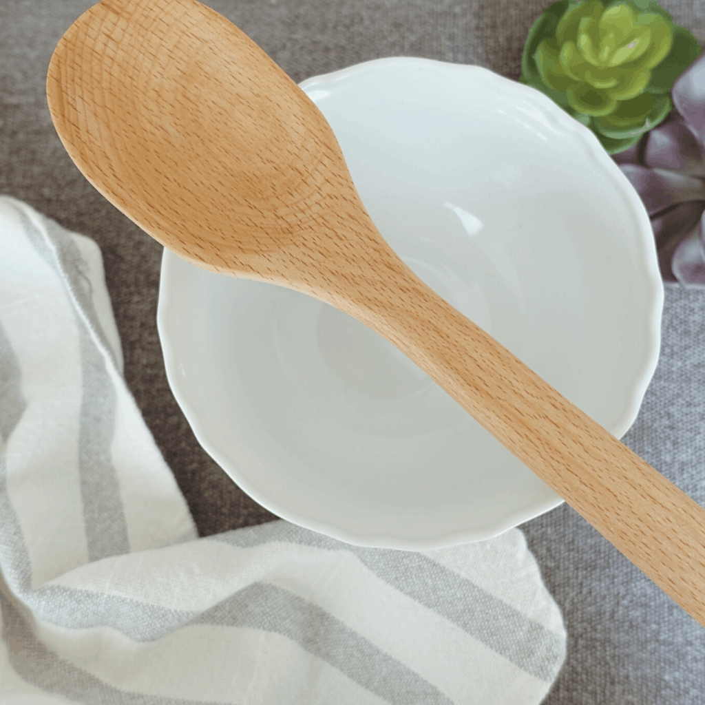 seasoned wooden spoon over white bowl with tea towel and succulents in background