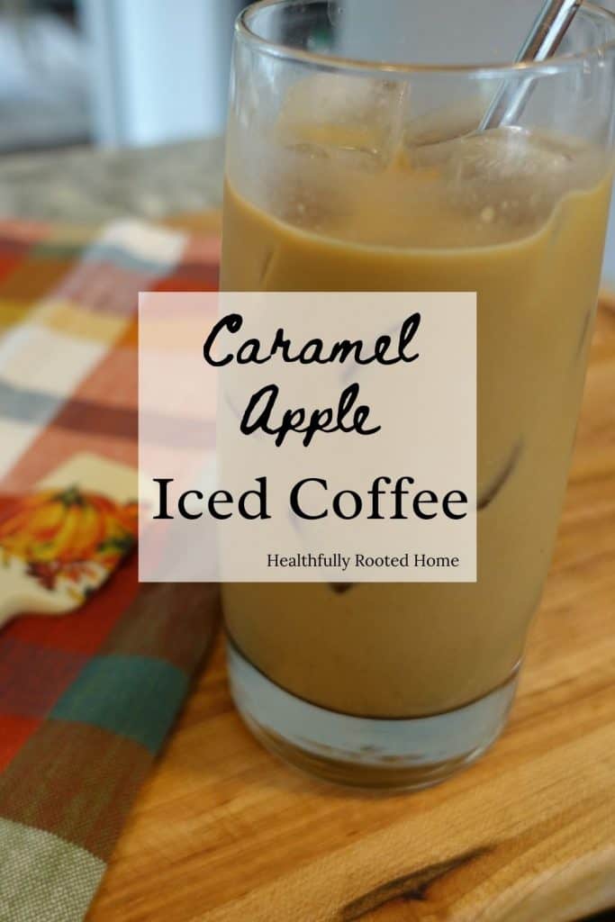 caramel apple iced fall coffee drink in a glass cup with a stainless steel straw next to a spatula with a pumpkin on it 