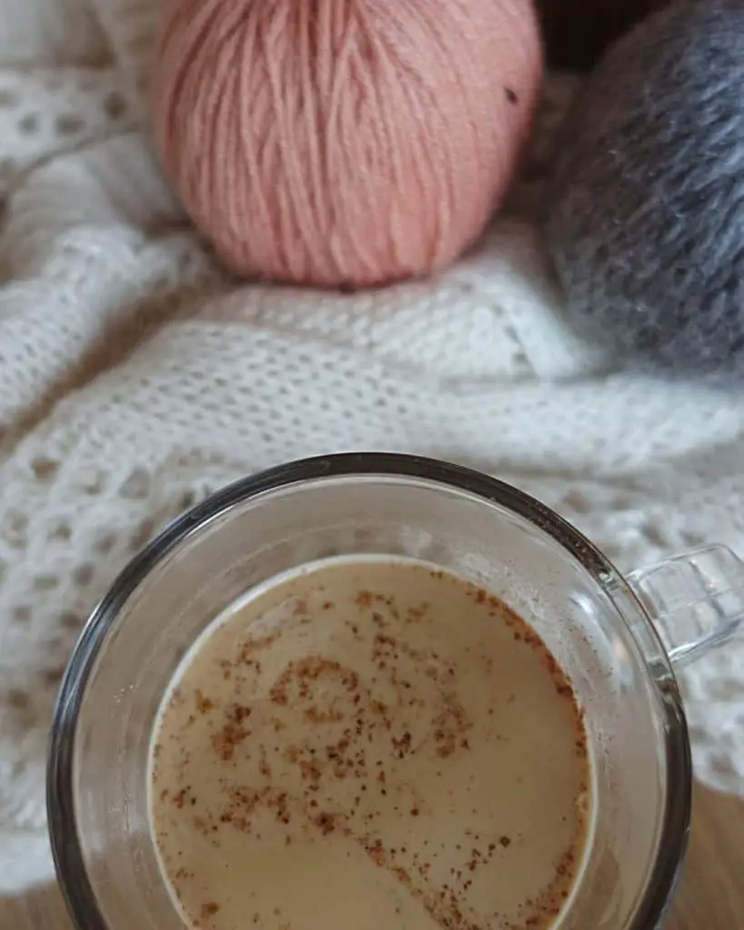 fall coffee drink maple pecan latte with a cozy sweater and sweater pumpkins in a glass coffee cup with cinnamon sprinkled on top