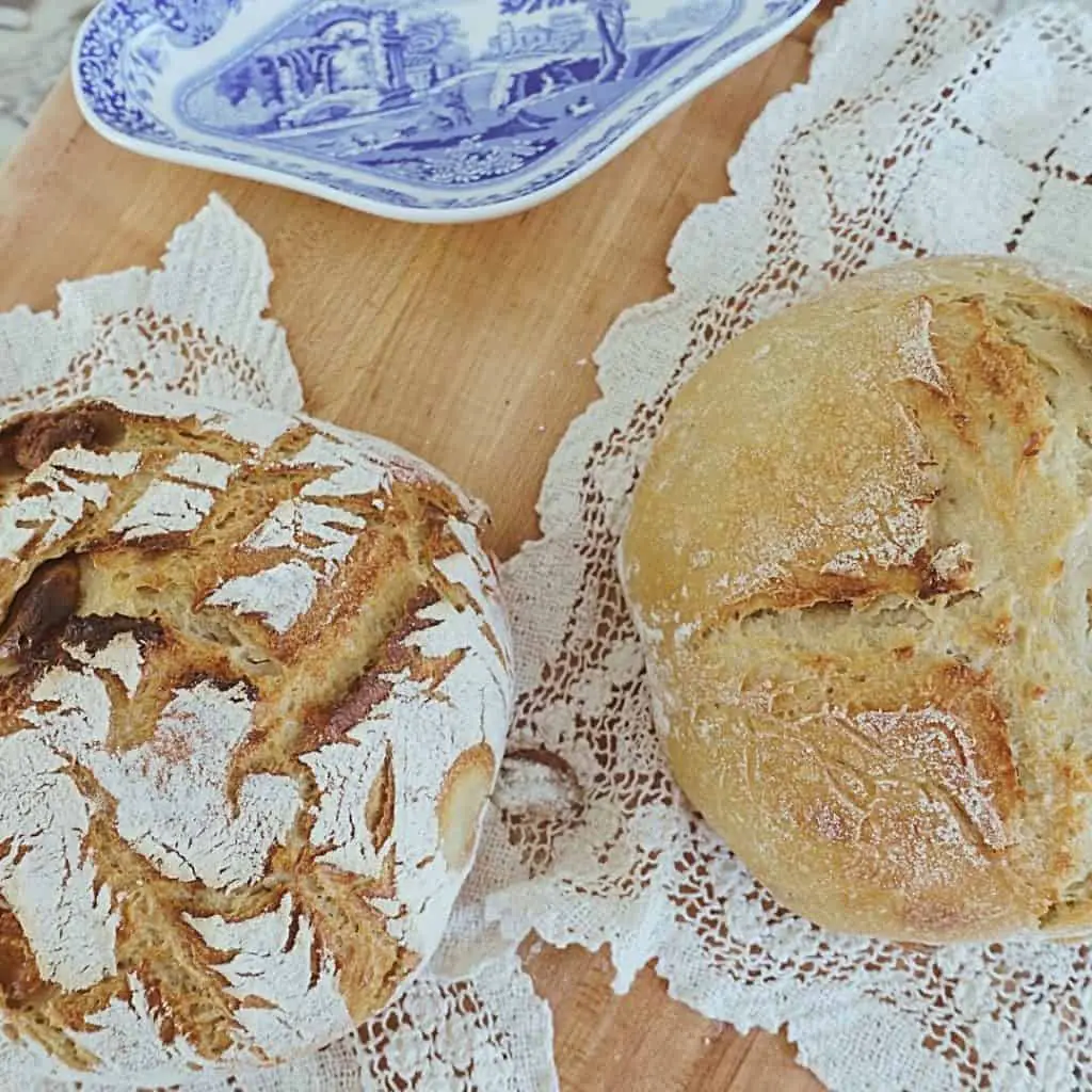 2 loaves of sourdough bread with lattice scoring pattern and cross scoring pattern on lace doilies and blue and white china in background