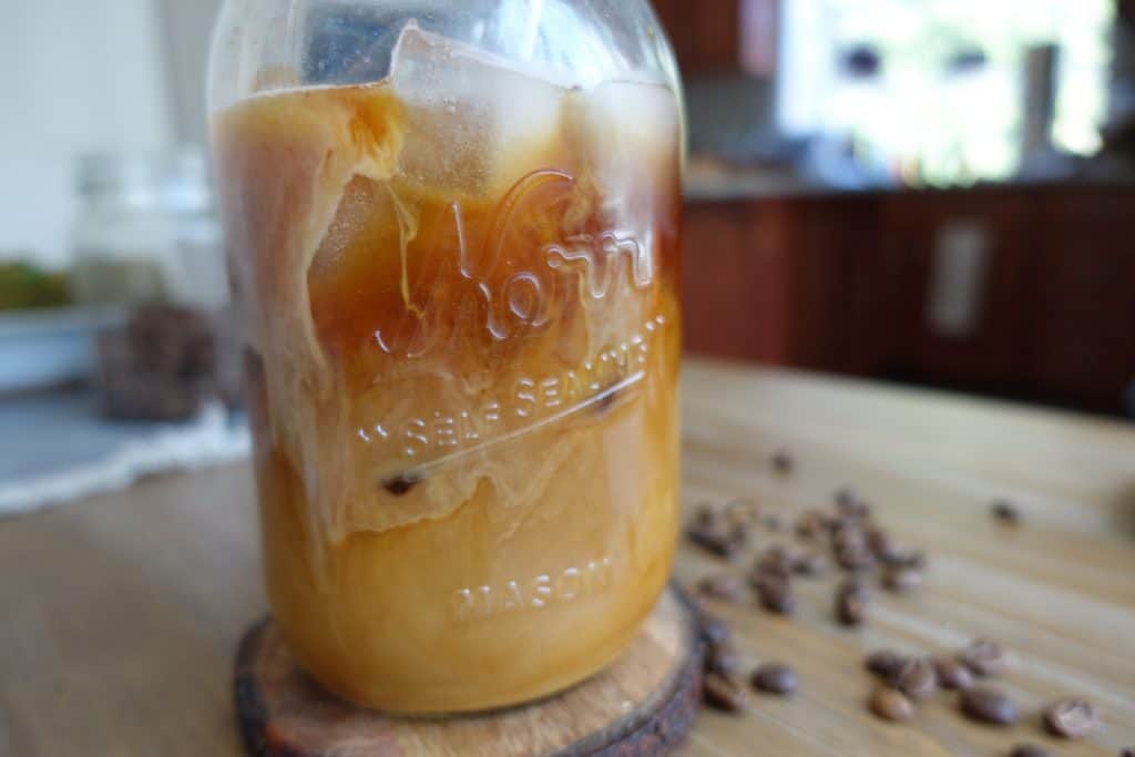 iced coffee with cream in mason jar with coffee beans surrounding it