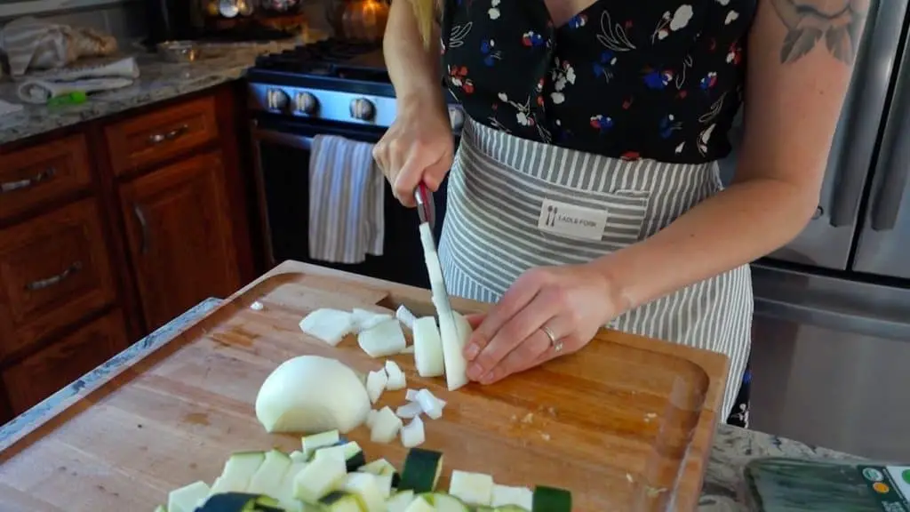 chopping onions with chefs knife on boos block cutting board wearing striped apron