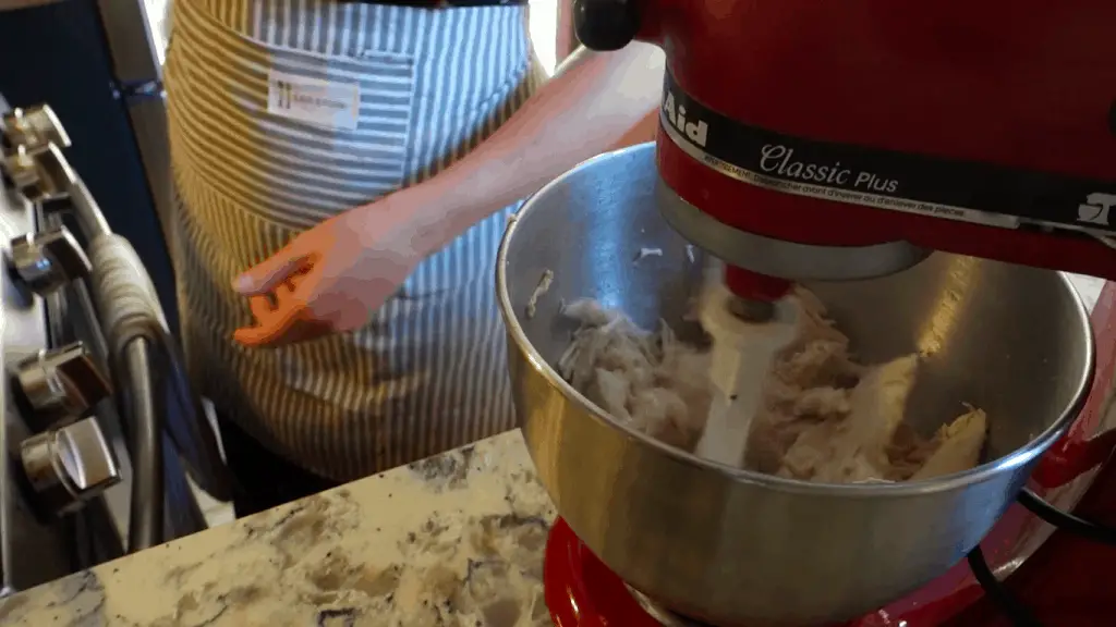 using kitchenaid to shred chicken for lemon chicken gnocchi soup wearing striped apron
