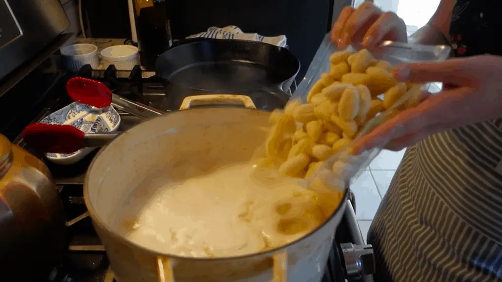 tossing gnocchi into boiling bone broth in a white dutch oven for lemon chicken gnocchi soup