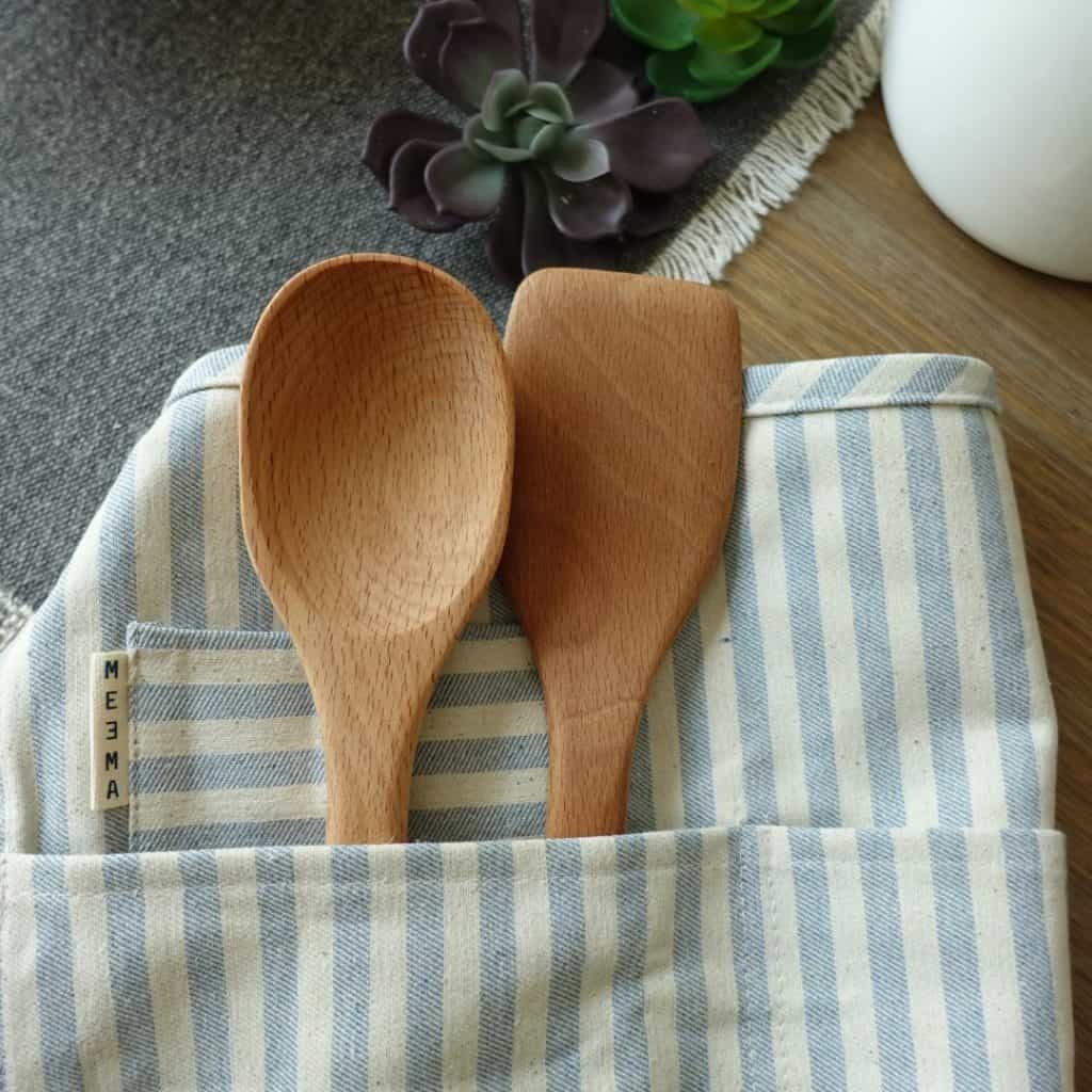 seasoned wooden spoons inside pocket of striped apron