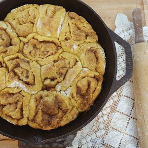 Healthfully rooted home pumpkin sourdough cinnamon rolls made in a cast iron skillet with rolling pin and doily