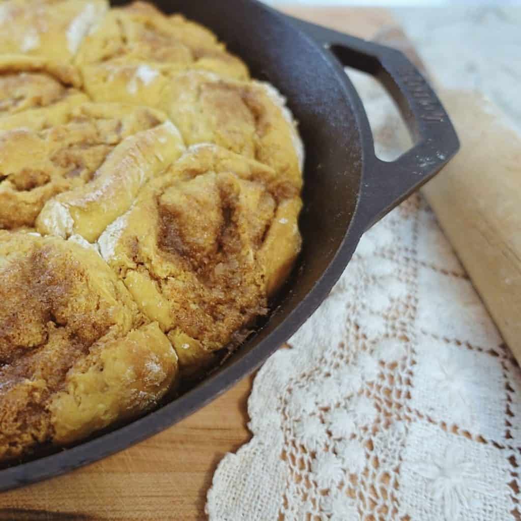 pumpkin sourdough cinnamon rolls in a cast iron skillet with doily and wooden rolling pin