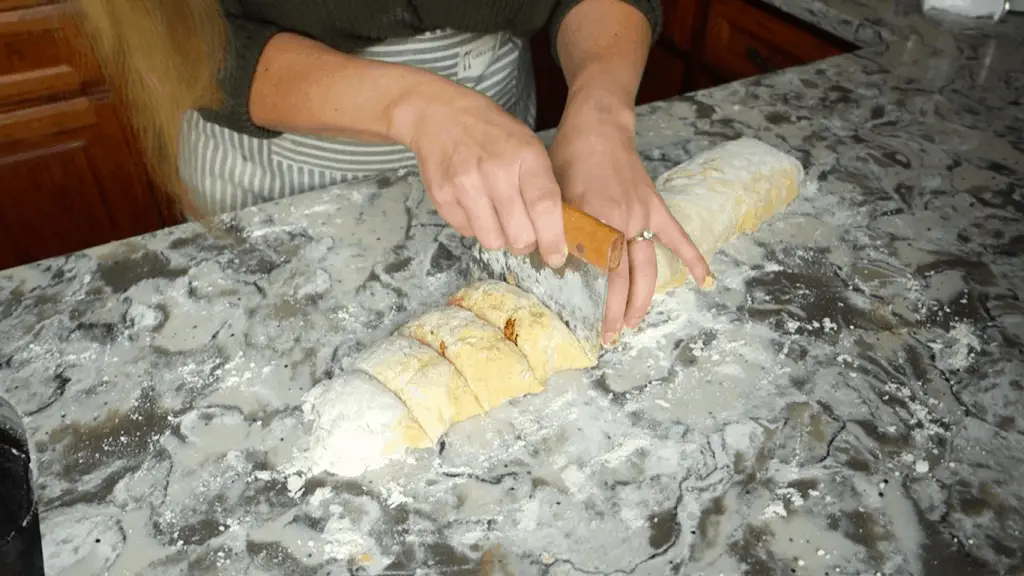 slicing pumpkin sourdough cinnamon roll dough into equal pieces using a dough scraper