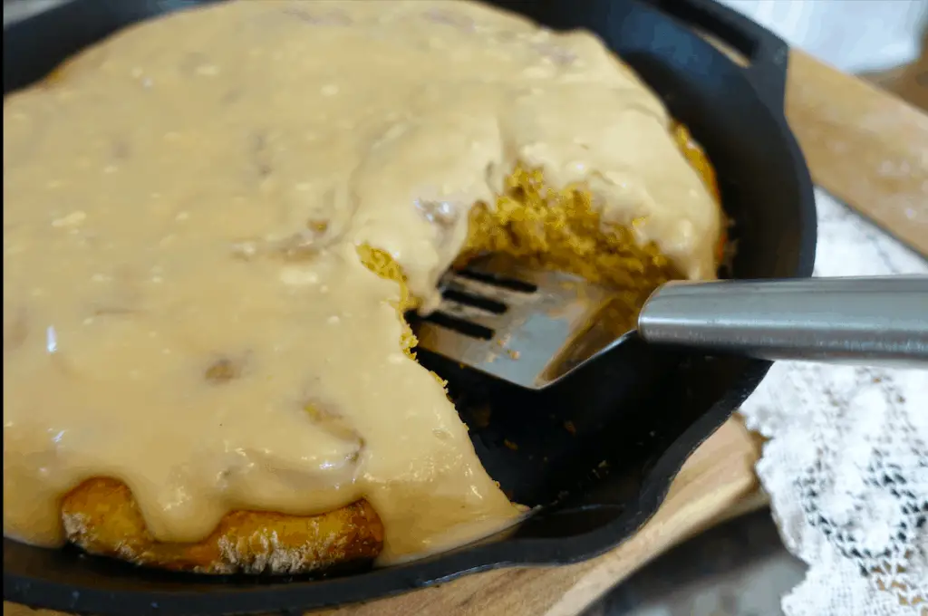 pumpkin sourdough cinnamon rolls with maple pecan frosting in a cast iron skillet and a stainless steel spatula