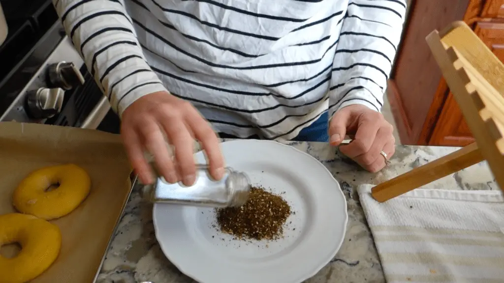 pouring zaatar seasoning blend onto a white plate with striped white and black shirt