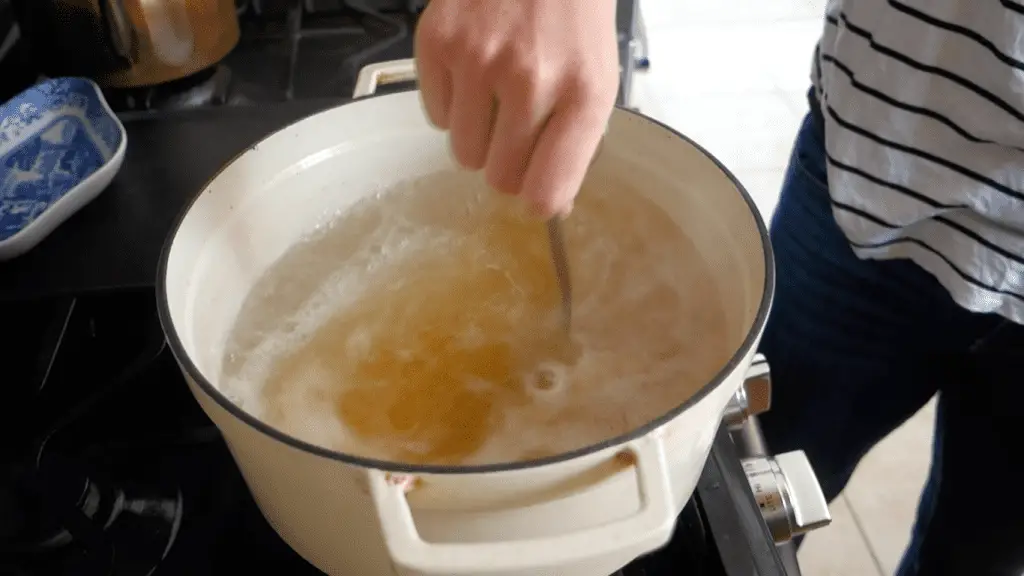 mixing baking soda and molasses into a pot of boiling water in a white dutch oven on a gas stove with a blue and white china bowl in the background and a copper tea pot