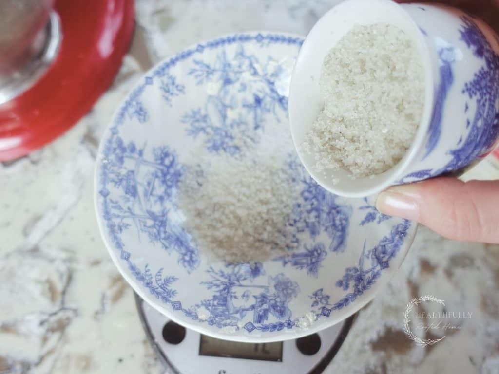 pouring sea salt from a blue and white china bowl into a larger blue and white china bowl on a kitchen scale