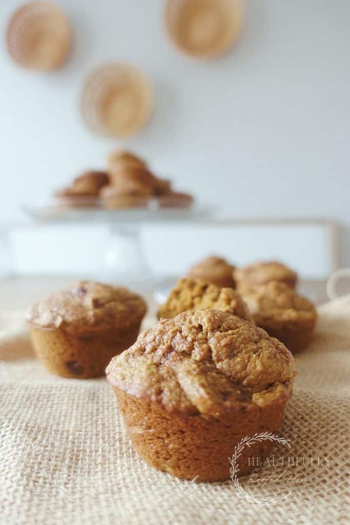sourdough pumpkin muffins sitting on burlap with cake stand in back