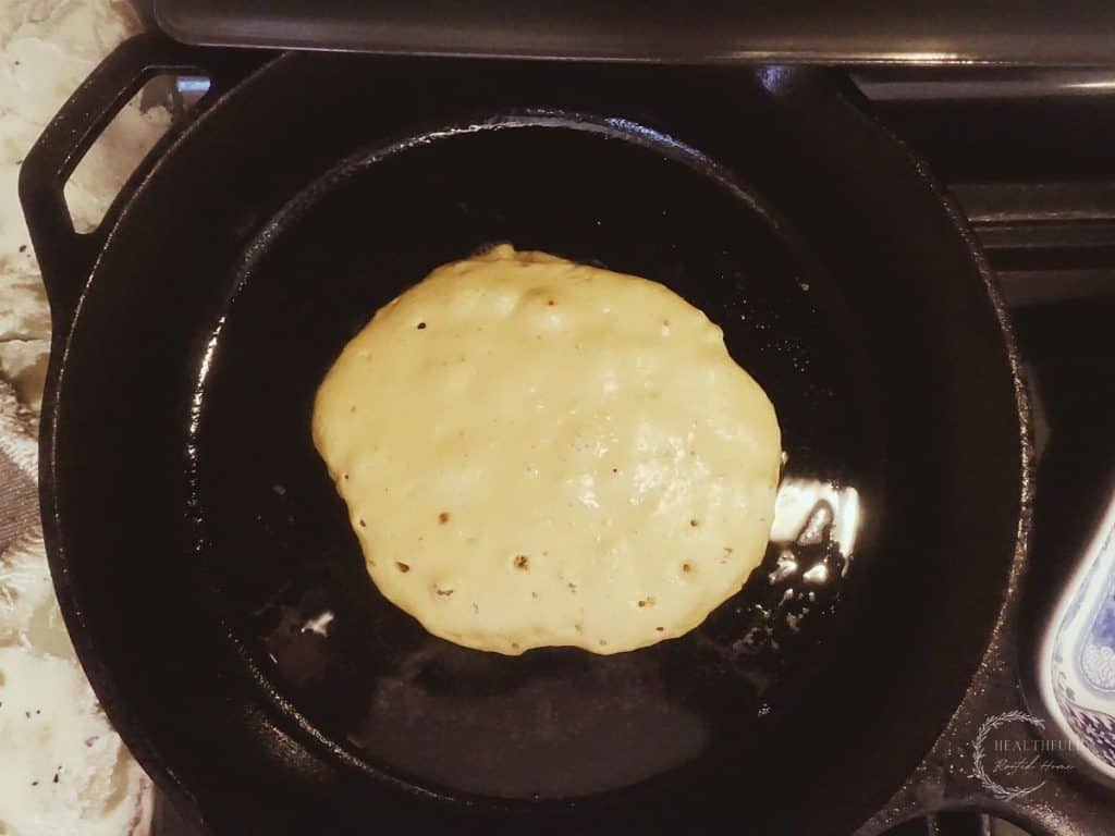 cast iron skillet with pancake ready to be flipped with bubbles on the surface