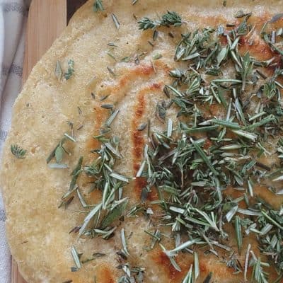sourdough discard flatbread with dried herbs on top next to a blue and white striped tea towel