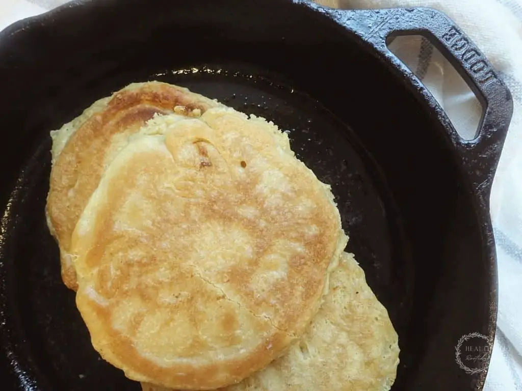 sourdough pancakes in a cast iron skillet with a blue and white striped tea towel in back