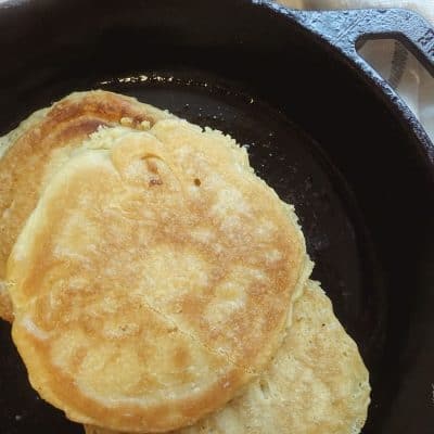 sourdough pancakes in a cast iron skillet with a blue and white striped tea towel in back