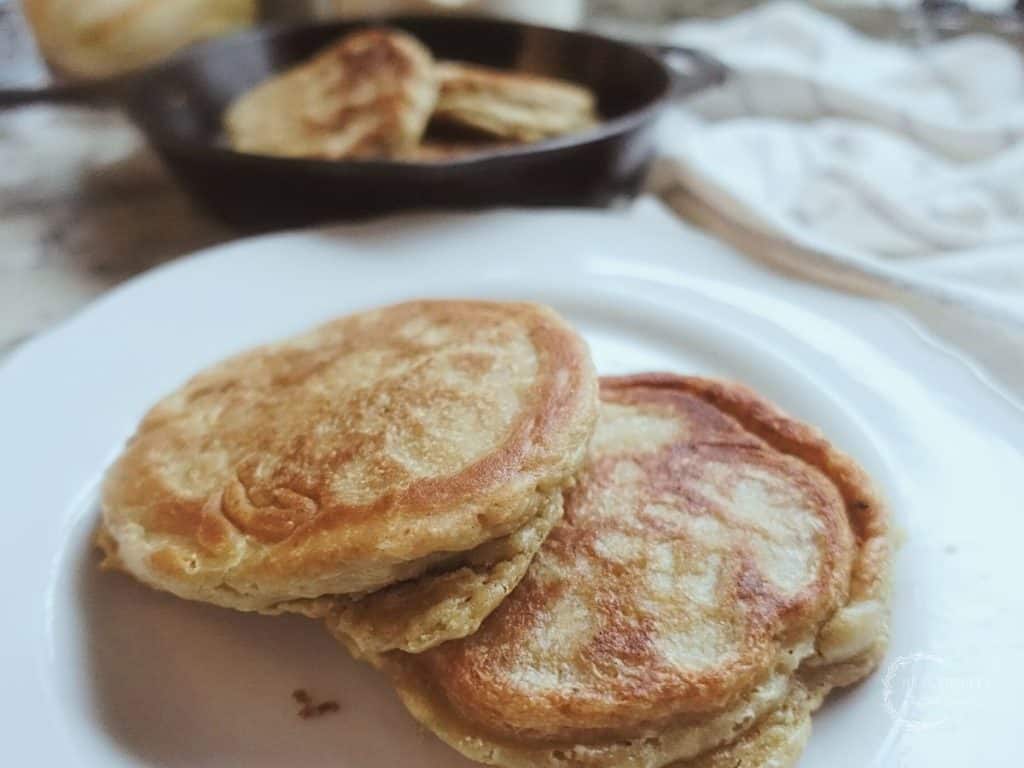 sourdough pancakes sitting on a white plate with a cast iron skillet in the back