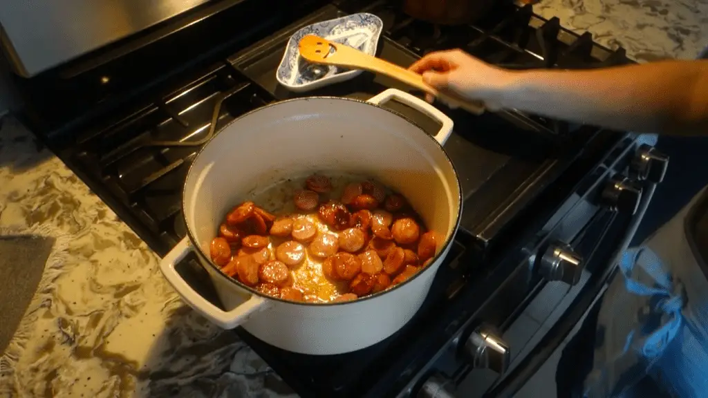 sausage browning in a white dutch oven with wooden spoon in back