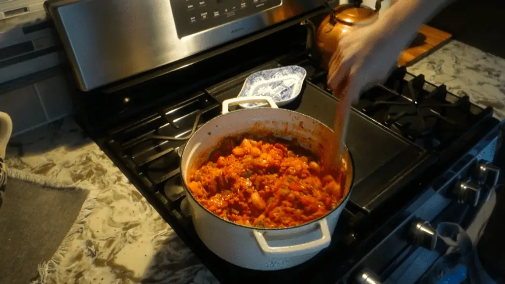 stirring jambalaya in a white dutch oven with a wooden spoon