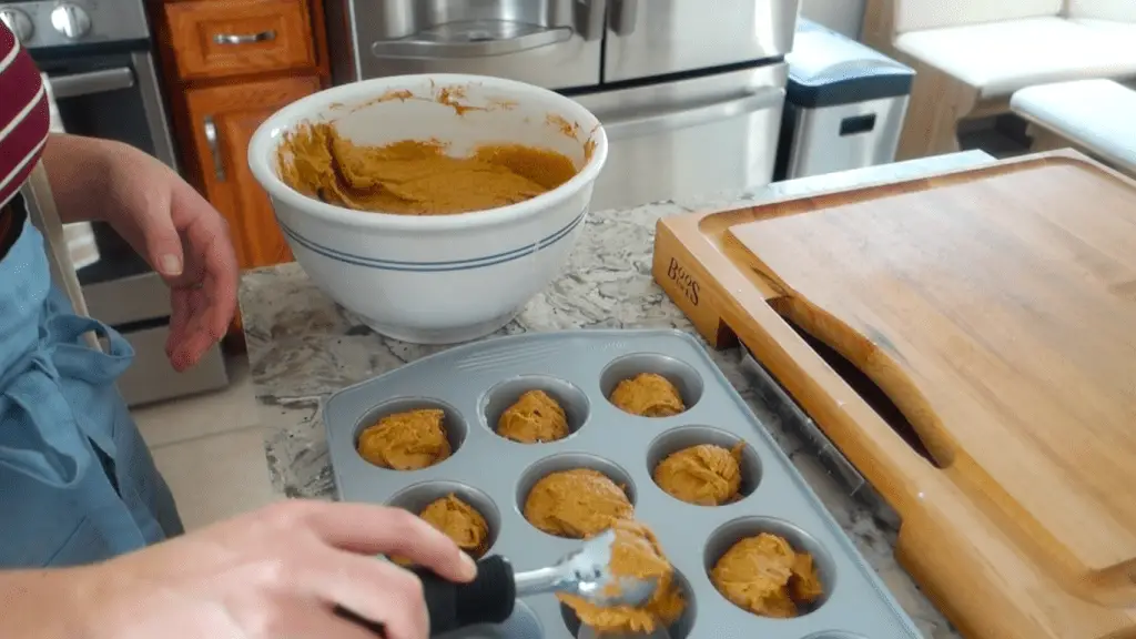 using an ice cream scoop to fill muffin tin with muffin batter