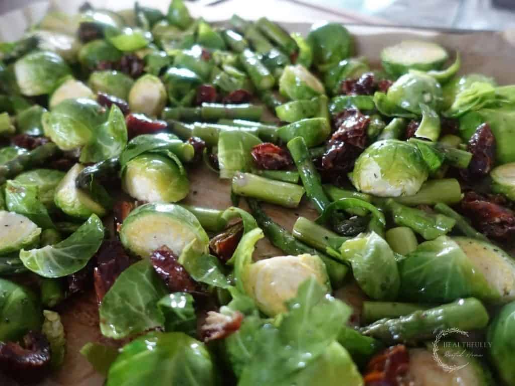 raw asparagus and brussels sprouts with dates poured on a baking sheet with parchment paper