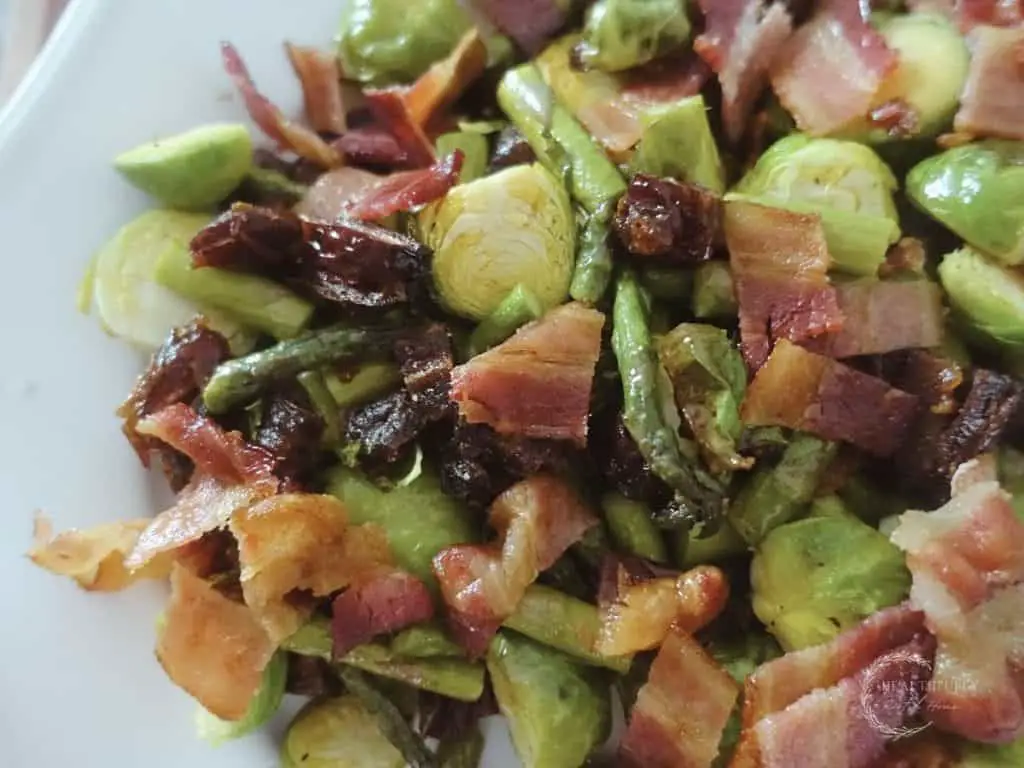 roasted asparagus and brussels sprouts with dates and bacon served on a white platter