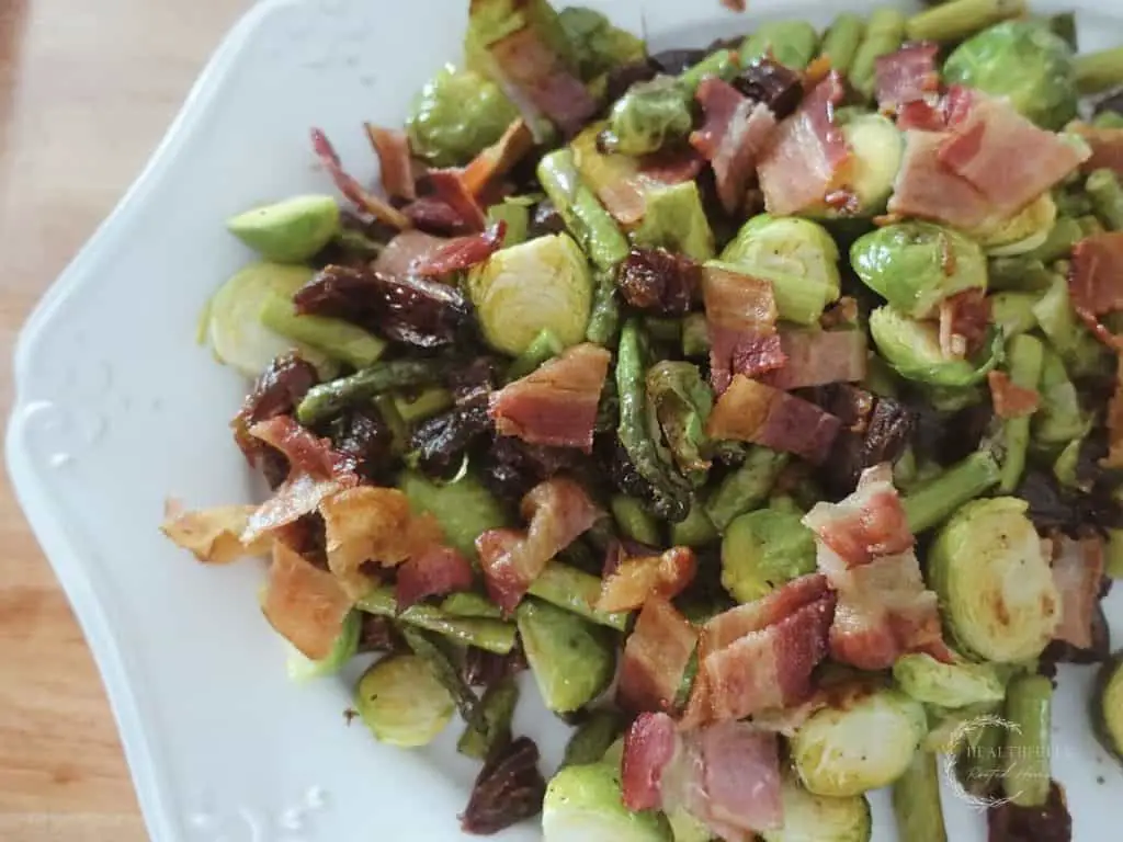 roasted asparagus and brussels sprouts with dates and bacon on a white serving tray