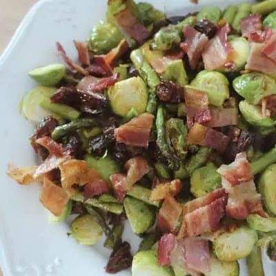 roasted asparagus and brussels sprouts with dates and bacon on a white serving tray