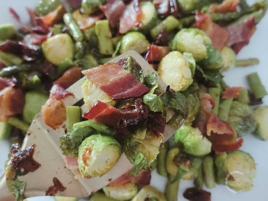 roasted asparagus and brussels sprouts with dates and bacon being served with a golden spatula