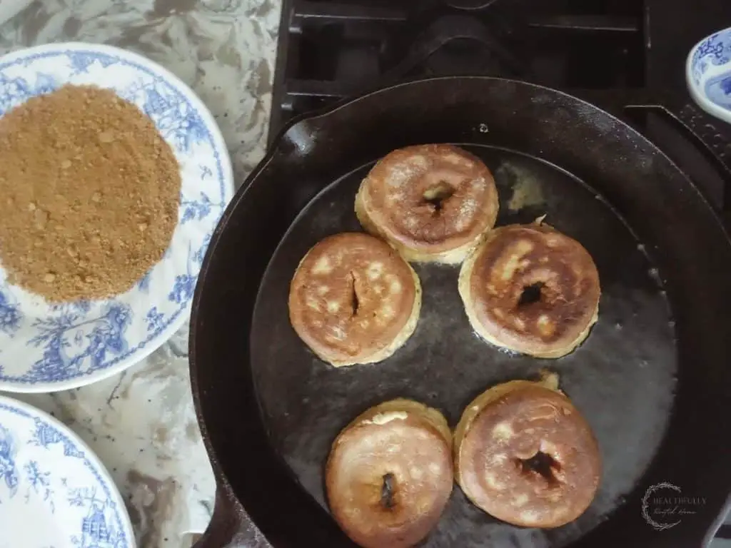 browned sourdough donuts frying on a cast iron skillet next to a blue and white plate with cinnamon sugar