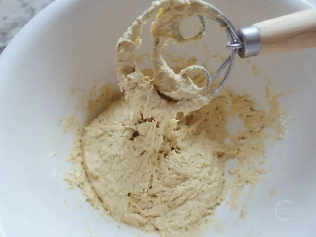 sticky sourdough dumpling batter falling from a danish dough whisk into a ceramic bowl with more batter