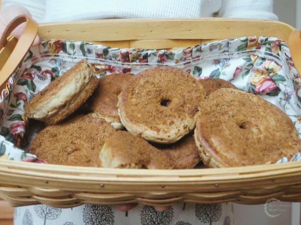 sourdough donuts with cinnamon sugar in a basket with floral liner and woman holding with a white sweater and apron