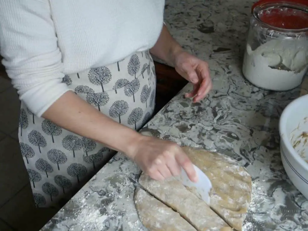 using a dough scraper to slice dough on a granite countertop with a glass jar of flour in the background