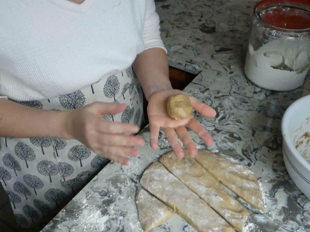 ball of dough in hand with dough in strips on the counter with a glass jar of flour in the background