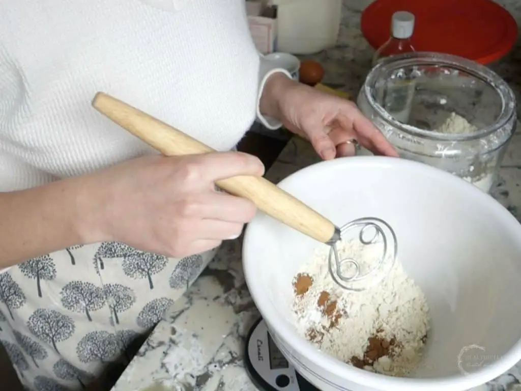 mixing dry ingredients in a large ceramic bowl with a danish dough whisk
