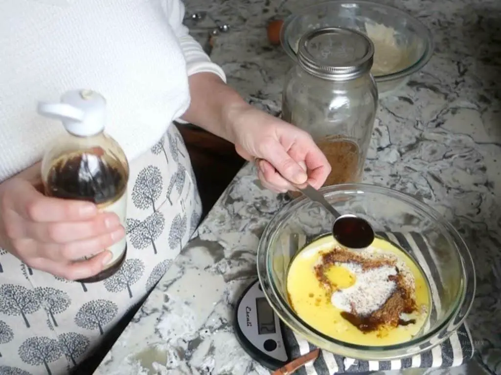 mixing wet ingredients in a glass bowl and adding vanilla extract wearing white sweater and apron