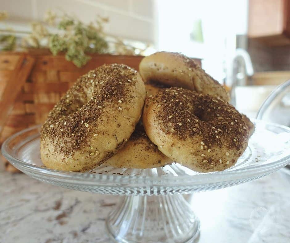 homemade zaatar bagels on a glass cakestand with a textured bottom on a granite countertop