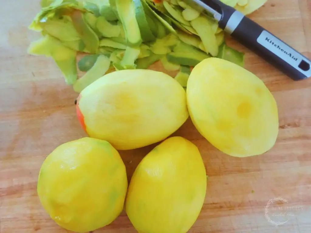 peeled mangos next to a peeler and mango peels